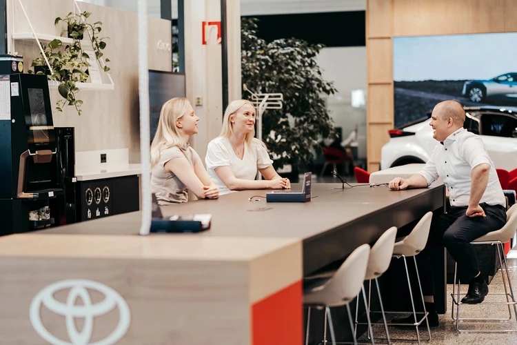 kolme ihmistä pitkän pöydän ääressä toyotan myymälässä